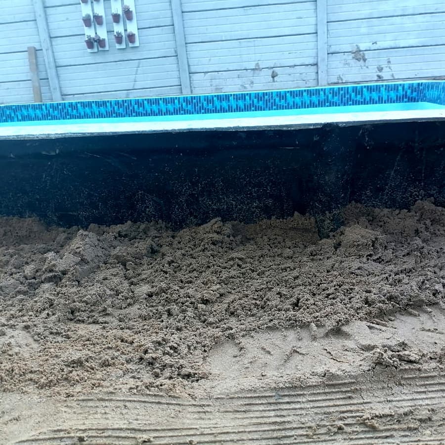 A pool build mid-construction: shell cast and coping laid, not yet filled