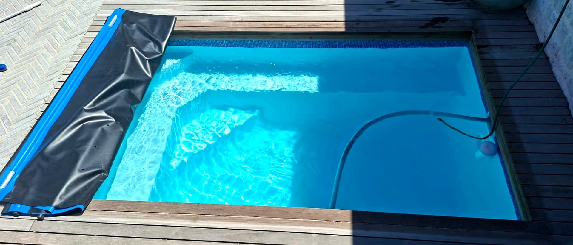 Sunlit pool with a timber deck and rolled-back cover, water perfectly balanced